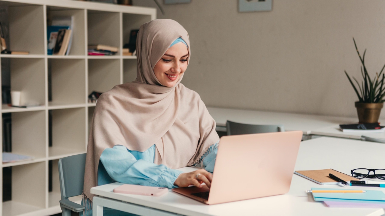 young pretty modern muslim woman in hijab working on laptop in office room, education online, remote work freelancer, typing thinking concentrated